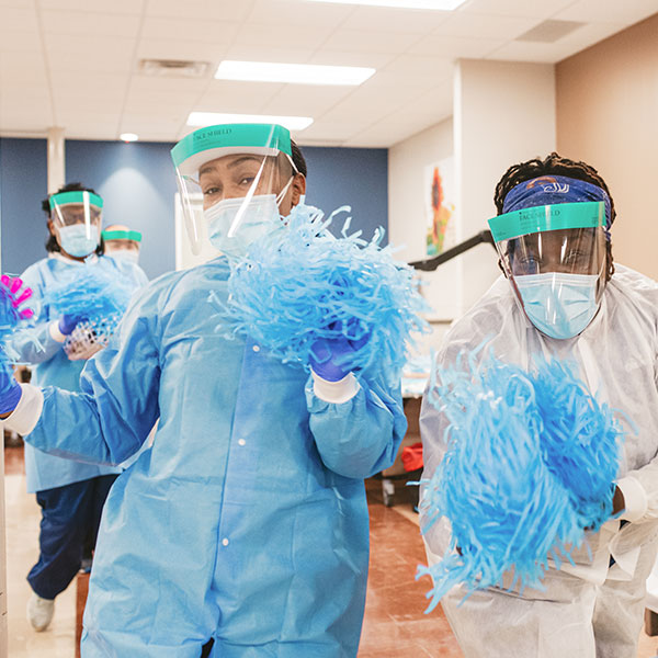 A group of individuals wearing protective gear, enthusiastically holding blue pom poms in a lively setting.