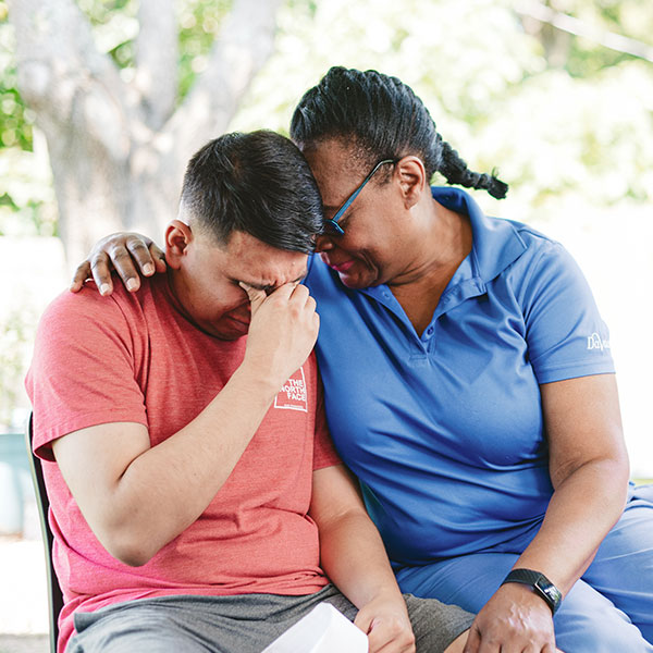 A woman and a man are seated together on a bench, engaged in conversation in a serene outdoor setting.